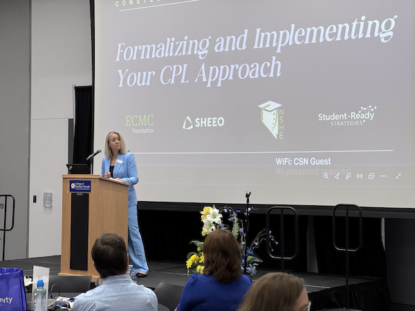A person in a blue suit stands at a podium presenting a session titled "Formalizing and Implementing Your CPL Approach" to an audience.