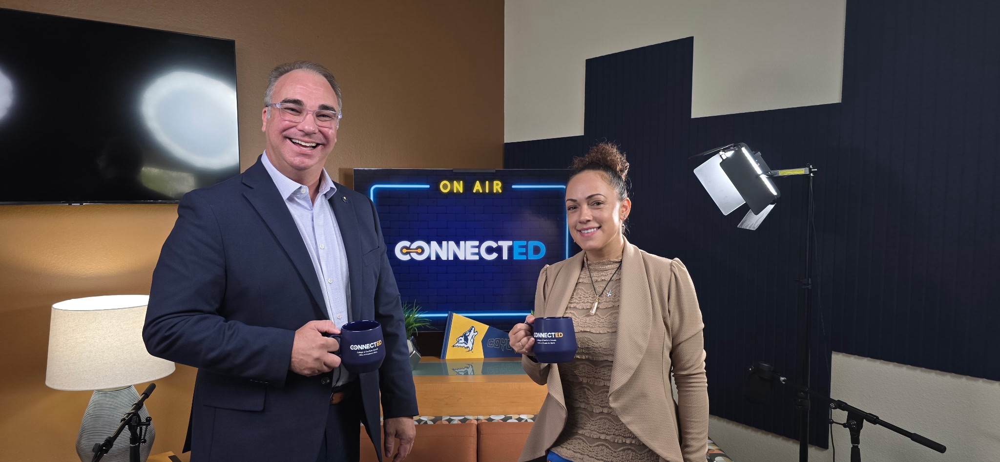 Two individuals stand in a studio setting holding branded mugs, with a screen displaying “ON AIR” and “CONNECTED” behind them.